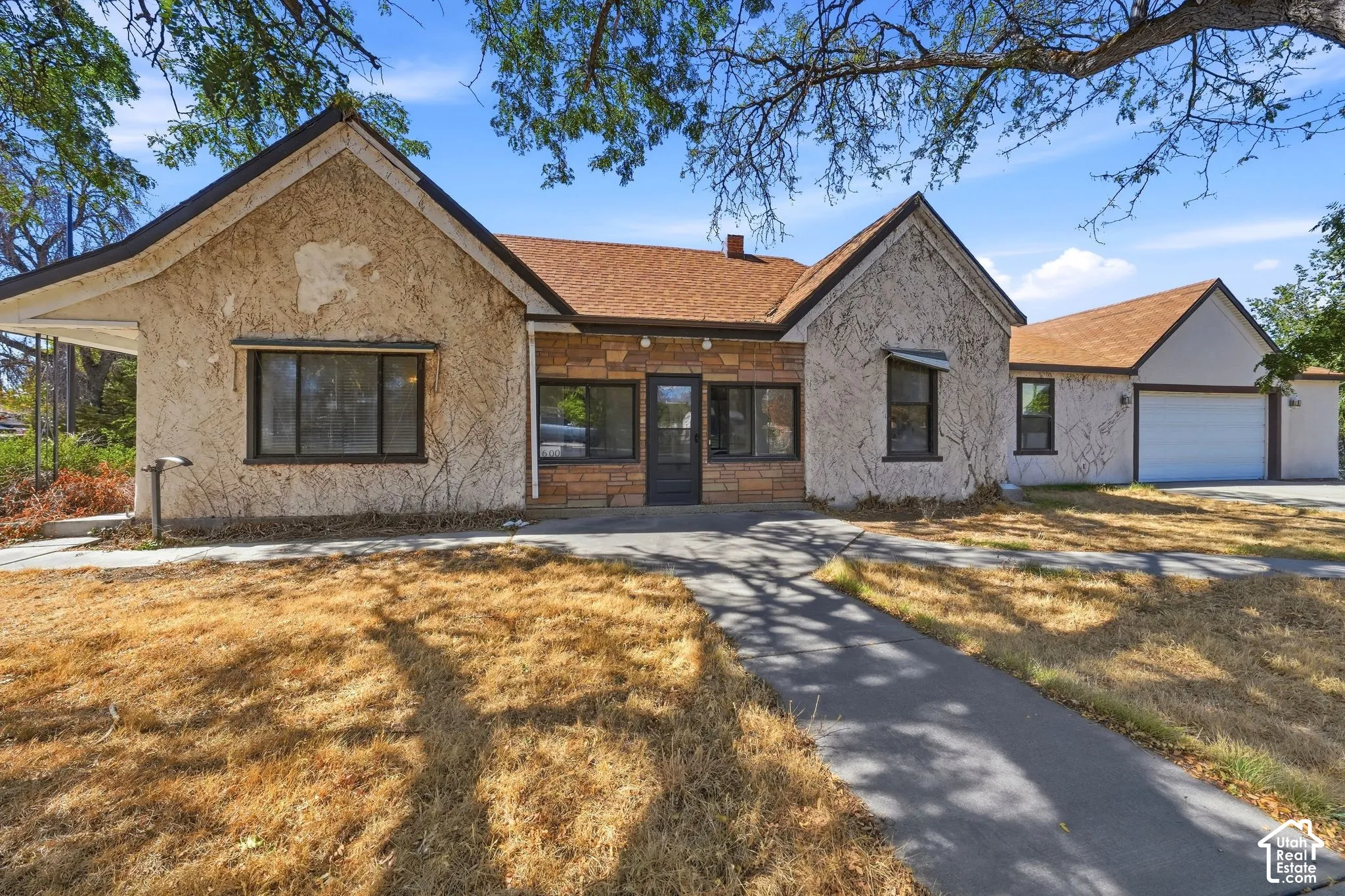 Stucco and stone facade, gabled roofline, attached garage, and paved walkway