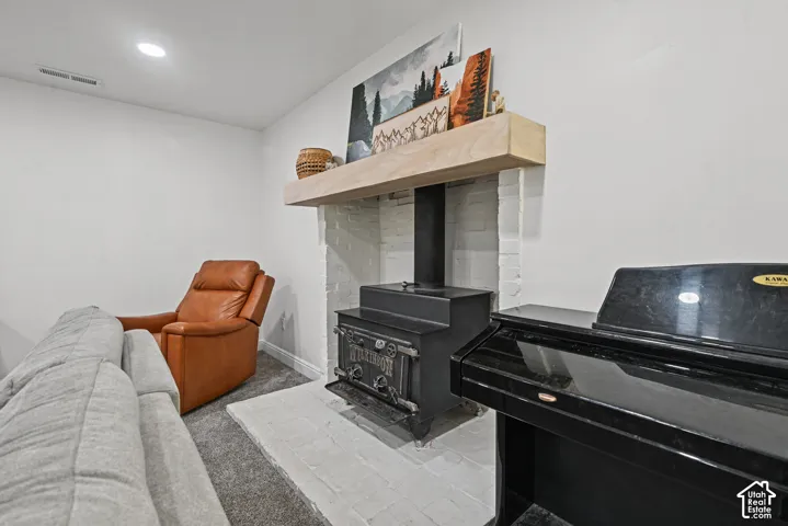 White painted brick fireplace featuring a wood-burning stove and a wood mantel