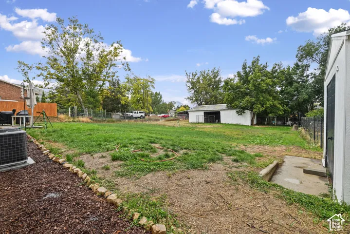 Expansive backyard with a large grassy area, mature trees, and a utility shed