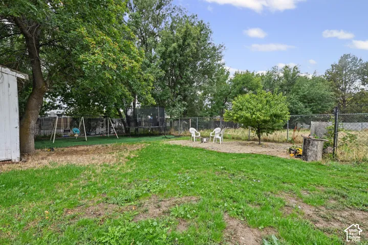 Expansive backyard with a mix of natural grass and artificial turf, mature trees, and chain-link fencing