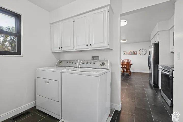 Laundry area featuring white cabinetry, a window with black trim, and dark tile flooring
