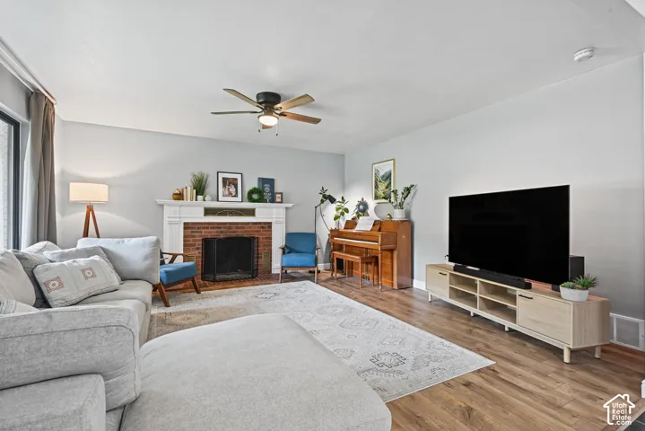 Brick fireplace with a white mantel, wood-finish flooring, and a ceiling fan