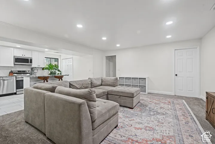 Recessed lighting illuminates the open-concept space featuring a kitchen with stainless steel appliances, white cabinetry, and a tile backsplash