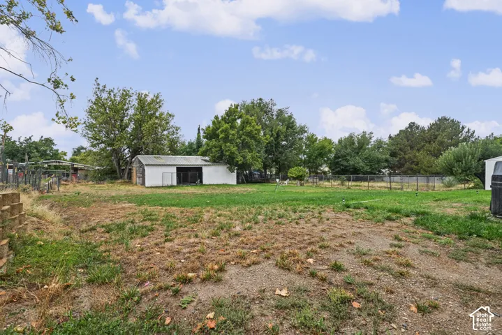 Expansive outdoor space featuring a detached storage structure, perimeter fencing, and mature trees