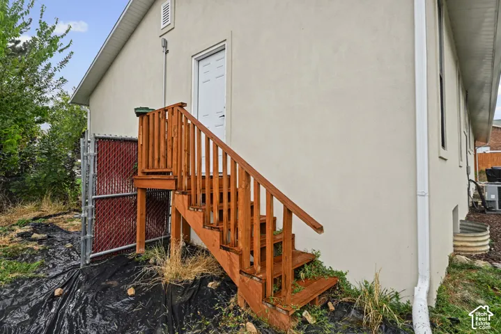 Exterior featuring a private entrance with wooden stairs, stucco siding, and a chain-link fence