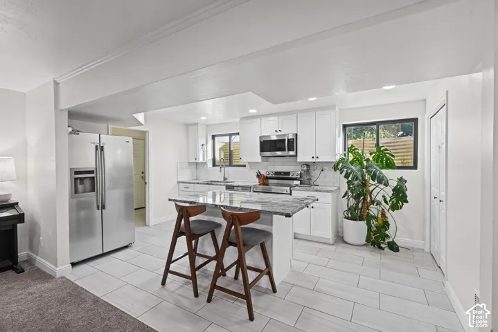 Kitchen featuring white cabinetry, stainless steel appliances, a center island with countertop seating, and light-toned tile flooring