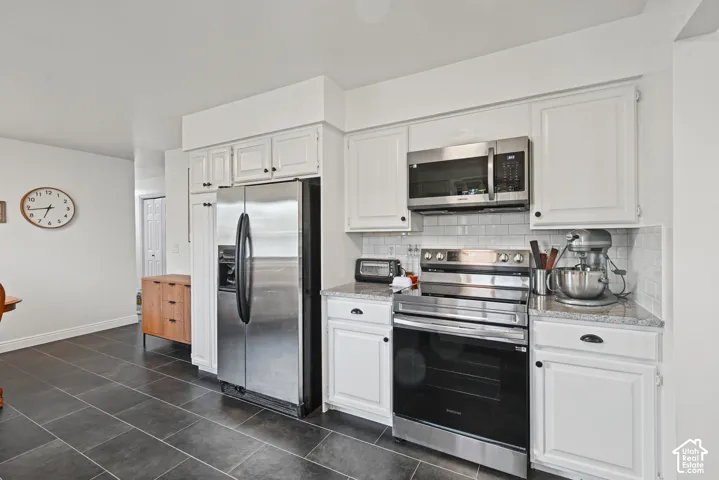 White cabinetry with black hardware, stainless steel appliances, granite-style countertops, white subway tile backsplash, and dark tile flooring