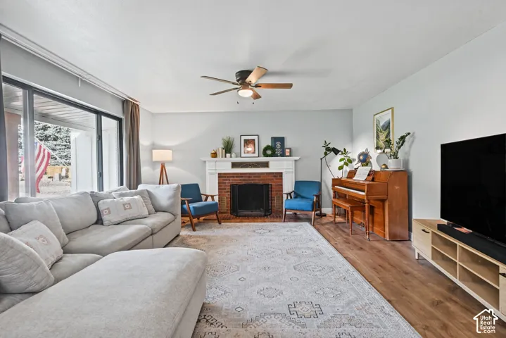 Brick fireplace with a white mantel, wood-finish flooring, and a ceiling fan