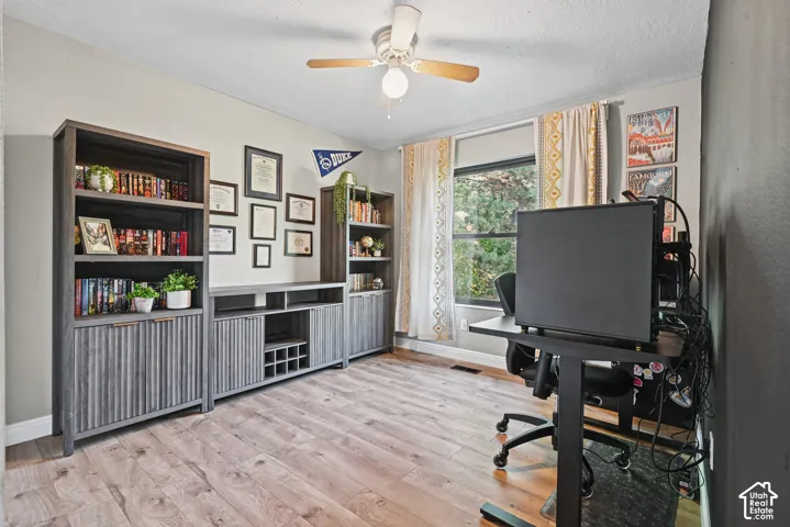 Wood-finish flooring, built-in shelving units, wall-mounted decor, and a ceiling fan with integrated lighting