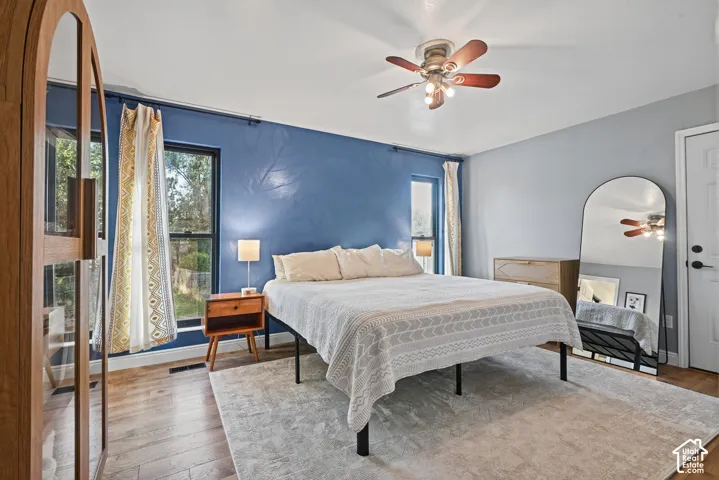 Wood-finish flooring with a ceiling fan, dual windows, and a white paneled door