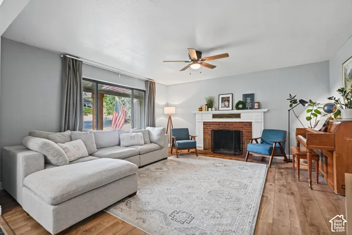 Wood-finish flooring, brick-surround fireplace with white mantel, ceiling fan, and large sliding glass door