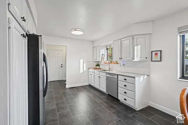 Dark-toned floor tiles, white cabinetry with dark hardware, white subway tile backsplash, light-toned countertops, and a stainless steel dishwasher