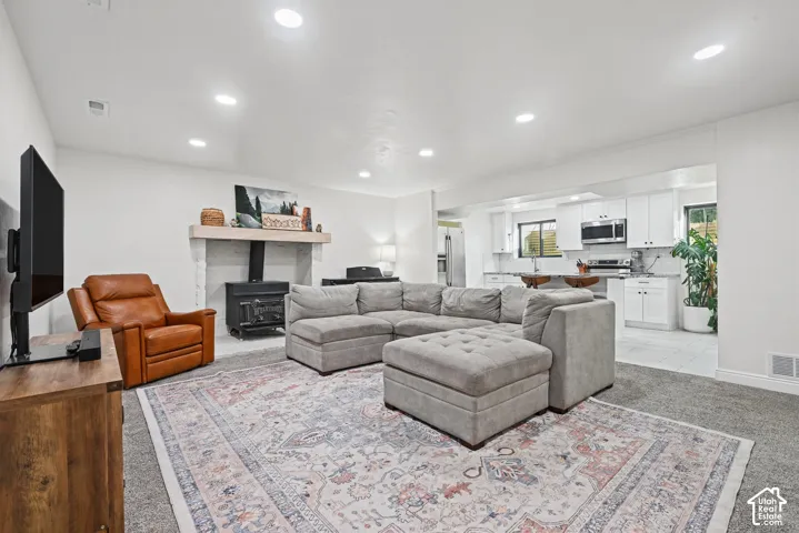 Open-concept living area with recessed lighting, a stone-faced fireplace with hearth, and a wood-burning stove