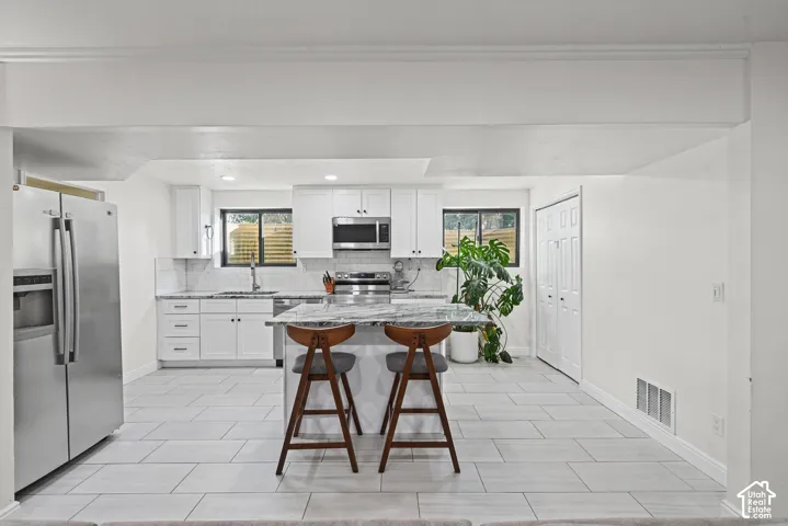 Contemporary kitchen featuring white cabinetry, stainless steel appliances, a center island with a marble-finish countertop, and large format tile flooring