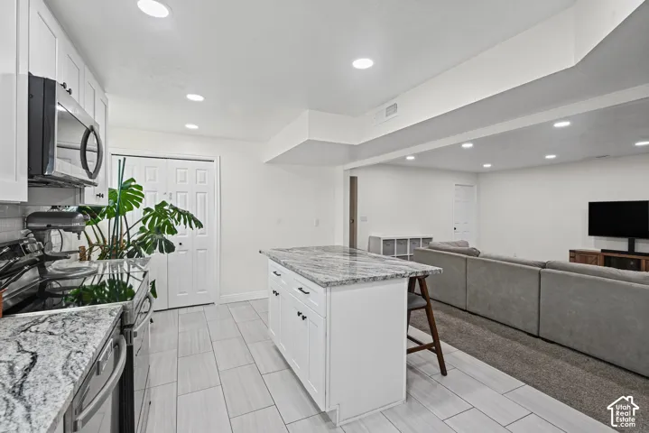 White cabinetry with dark hardware, stainless steel appliances, light-toned tile flooring, and recessed lighting