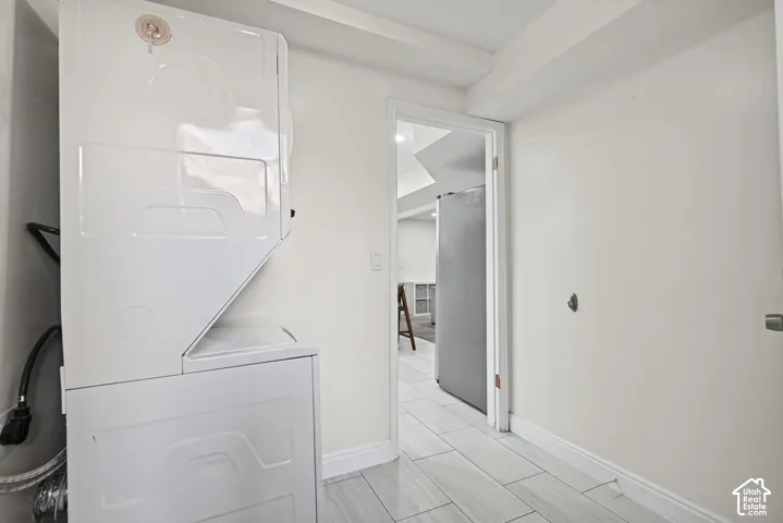 Stacked white laundry appliances, light-toned wood-finish flooring, and white baseboards