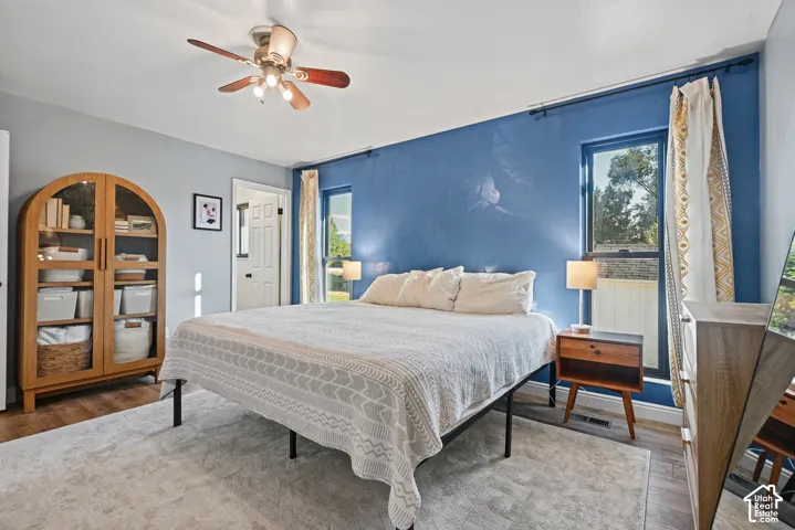 Recessed window openings, wood-finish flooring, ceiling fan with integrated lighting, a white painted door, and a built-in wall niche