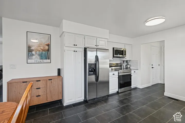 Stainless steel appliances, white cabinetry, dark large-format tile flooring, white subway tile backsplash, and recessed lighting
