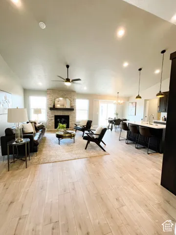 Vaulted ceilings with recessed lighting, stone-clad fireplace with mantel, wood-finish flooring, kitchen island with seating, and dark-finish cabinetry