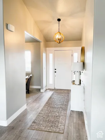 Vaulted ceiling entry with wood-finish flooring, white paneled entry door, and decorative hanging light fixture