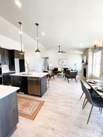 Vaulted ceilings, wood-finish flooring, stone fireplace, kitchen island with built-in sink, and pendant lighting