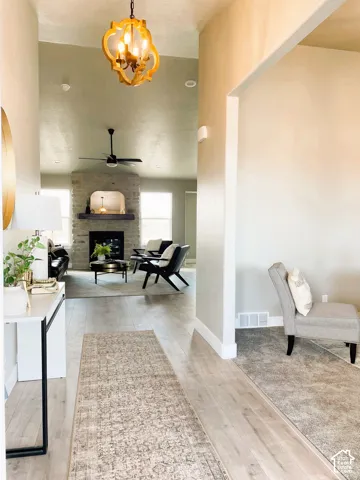 Vaulted ceiling, open architectural design, wood-finish flooring, stone fireplace, and a decorative chandelier