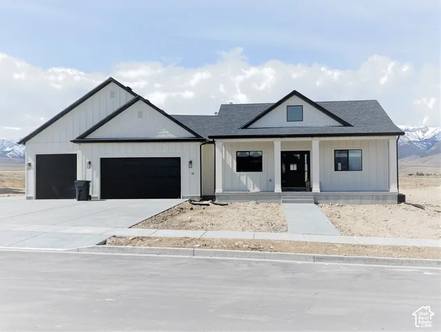 Modern farmhouse exterior with white vertical siding, black trim, a covered front porch, and a two-car garage