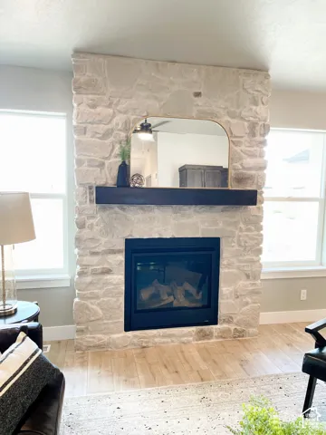Stone-clad fireplace with a dark wood mantel and a built-in firebox, complemented by light wood-finish flooring and multiple windows