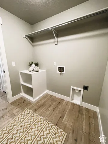 Laundry area featuring wood-finish flooring, a built-in shelving unit, and a clothing rod