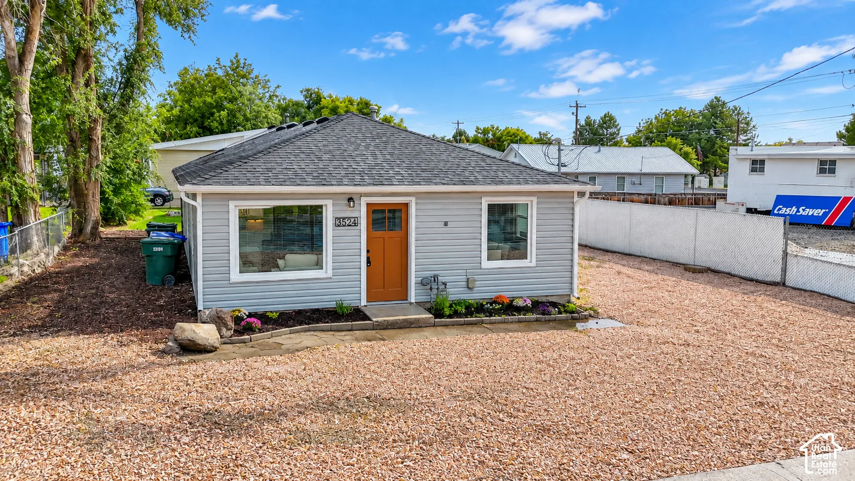 Gray siding exterior with a dark shingle roof, a wood-finish front door, and a gravel driveway