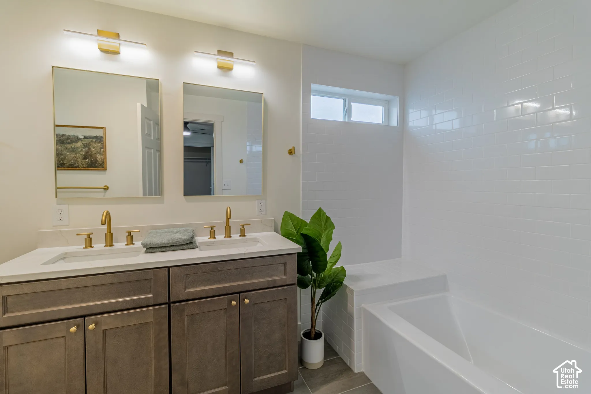 Double vanity with integrated sinks, brushed gold fixtures, a built-in bathtub, and white subway tile surround