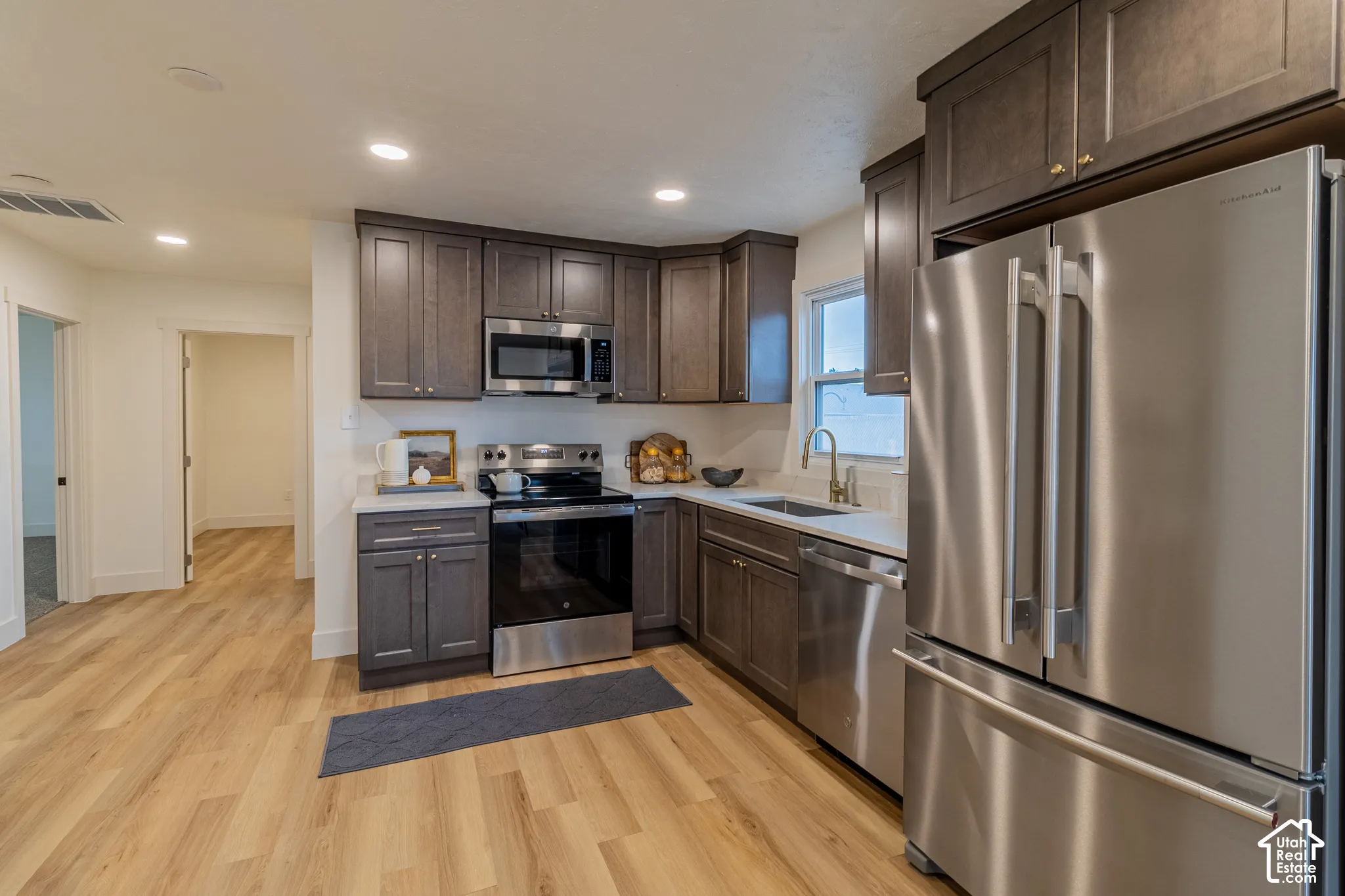 Kitchen featuring wood-finish flooring, dark wood-finish cabinetry, stainless steel appliances, white countertops, and recessed lighting