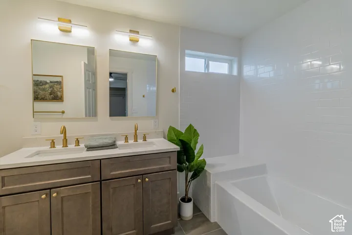 Double vanity with integrated sinks, brushed gold fixtures, a built-in bathtub, and white subway tile surround