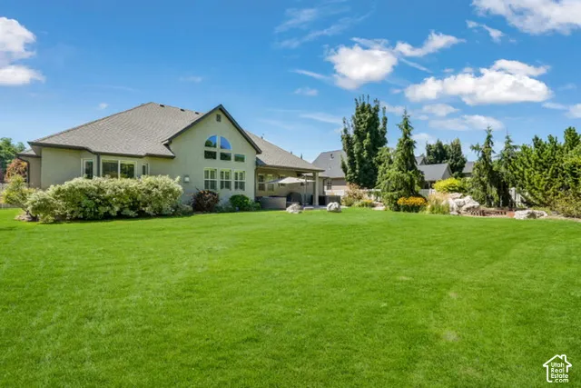 Expansive green lawn, mature trees, stucco exterior, covered patio, and large arched window