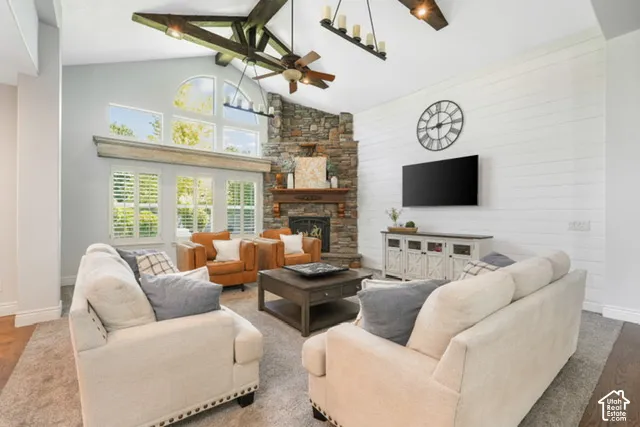 Vaulted ceiling with exposed beams, floor-to-ceiling stone fireplace, plantation shutters, and shiplap accent wall