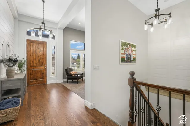 Hardwood flooring, wood-paneled accent wall, arched entryway with transom window, iron spindle staircase, and recessed lighting