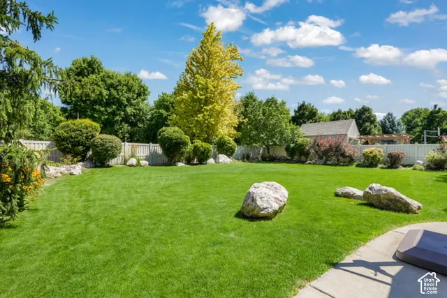 Expansive green lawn with mature landscaping, a white privacy fence, and decorative boulders