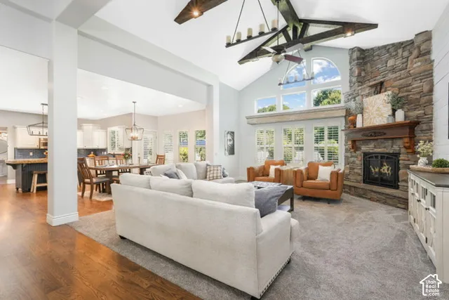 Living space featuring a vaulted ceiling with exposed beam chandelier, stone fireplace, and a wall of windows
