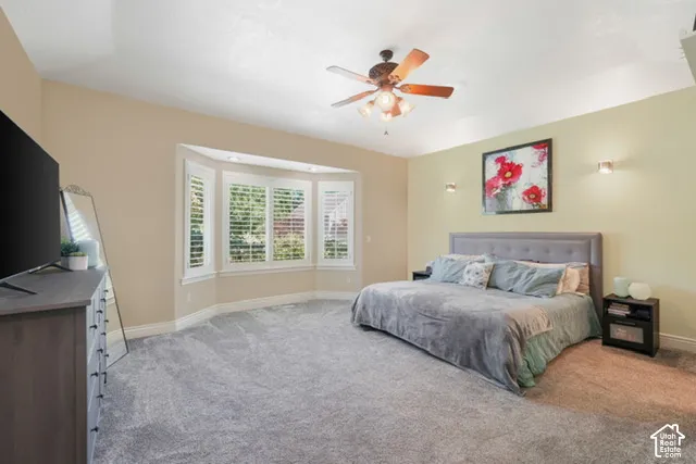 Vaulted ceilings, bay window with plantation shutters, ceiling fan with light fixture, wall-mounted sconces, and neutral wall tones