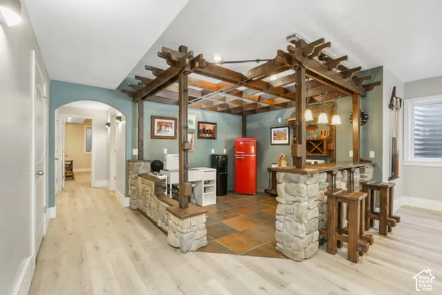 Entertainment area featuring a built-in bar with stone accents, wood-finish flooring, and an archway