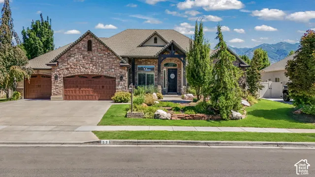Stone facade with a timber frame entry, arched garage doors, an expansive driveway, and established front landscaping
