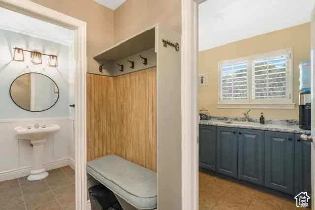 Pedestal sink with a circular mirror, wood-finish wall paneling, built-in bench with cushion, shaker-style cabinetry, and a countertop with an undermount sink