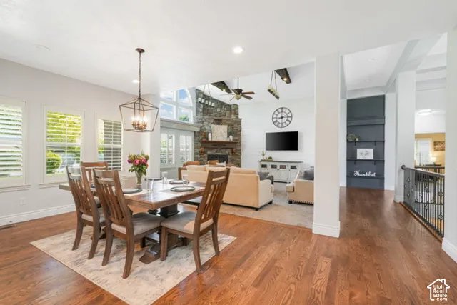 Hardwood flooring with a decorative pendant light fixture, plantation shutters, built-in shelving, and a stone-faced fireplace
