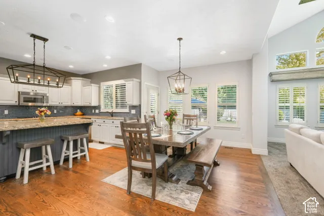 Open-concept living space featuring hardwood flooring, vaulted ceiling, white cabinetry with dark hardware, a tile backsplash, and a kitchen island with seating