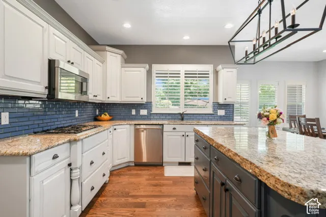 Kitchen featuring wood-finish flooring, light-toned cabinetry, a blue subway tile backsplash, stainless steel appliances, and a central island with a contrasting base