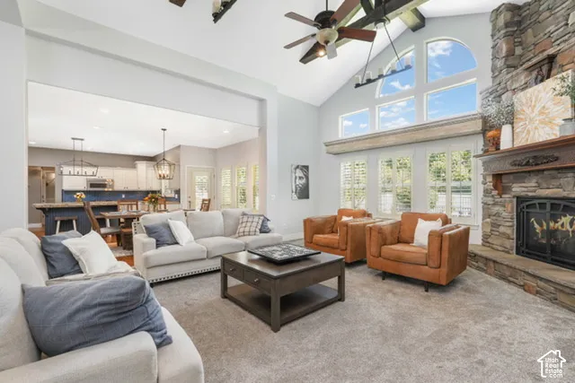 Vaulted ceiling with exposed beams, stone-clad fireplace, large windows with arch detail, and a built-in kitchen island