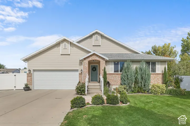 Exterior featuring brick accents, siding, a two-car garage, established landscaping, and a front lawn