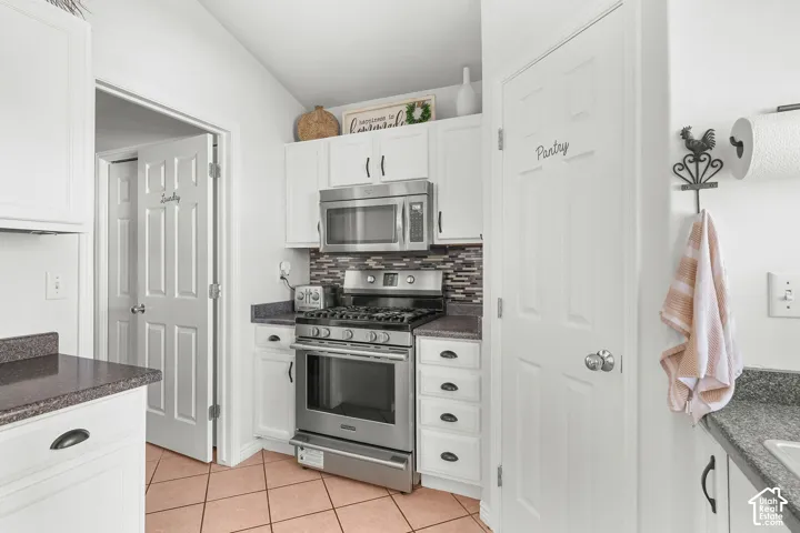 White cabinetry, stainless steel appliances, patterned backsplash, pantry storage, and tile flooring