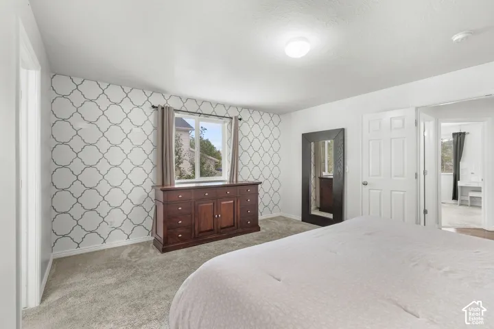Carpeted flooring, patterned accent wall, white painted walls, window with trim, and a ceiling light fixture