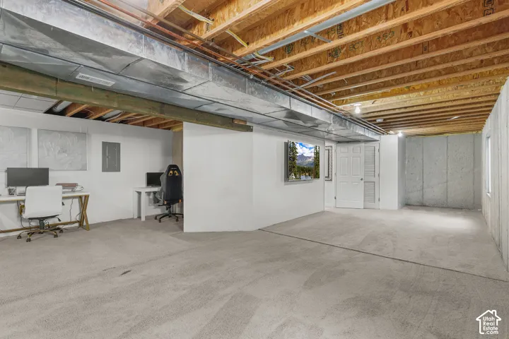 Unfinished lower level with exposed ceiling joists, concrete foundation walls, and light gray carpeting